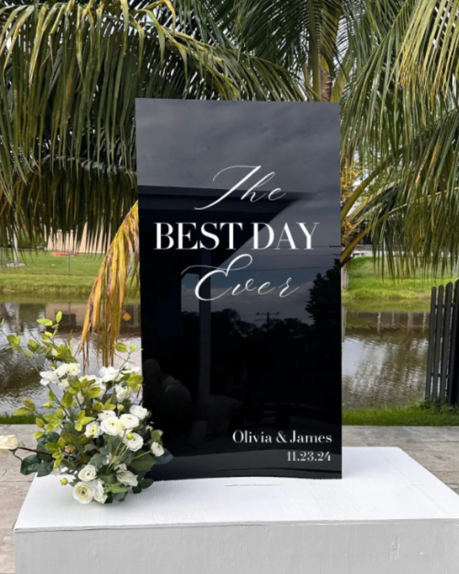 Dark wedding welcome sign with white lettering and floral accents.